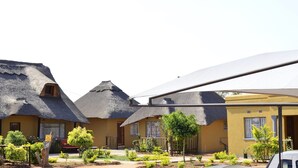 A row of thatched-roof cottages with a yellow exterior, a covered outdoor area, and a signboard.