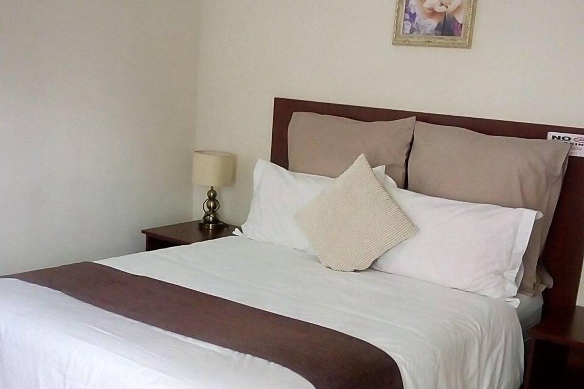 A neatly made bed with a brown bedspread, a white comforter, and two pillows.
