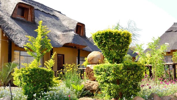 A traditional thatched-roof building with a well-maintained garden featuring various plants and flowers.