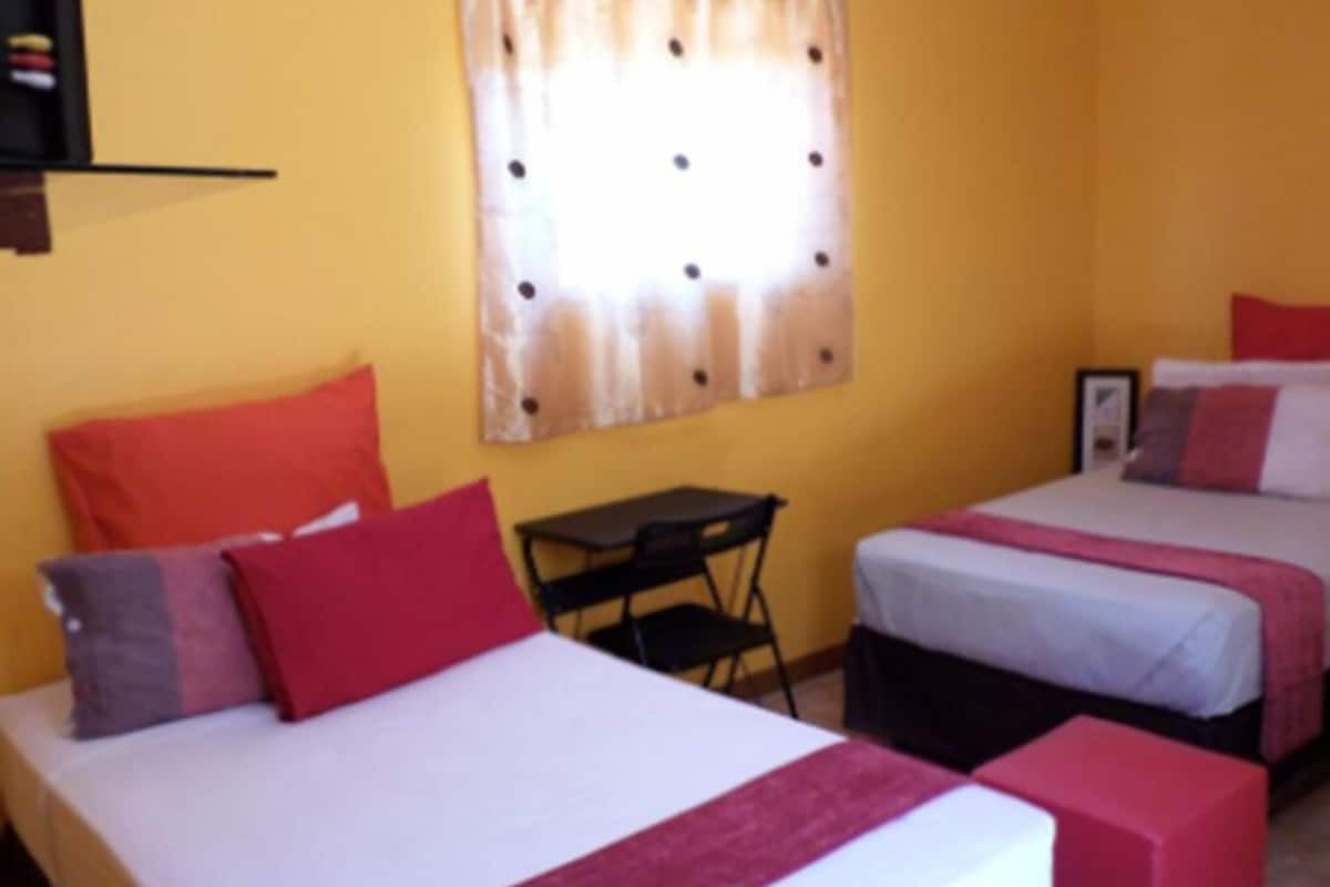 A hotel room with two beds, a small table, and a chair.