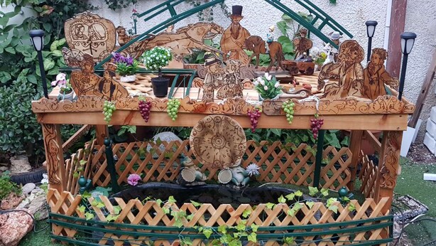 A wooden table with intricate carvings and a lattice base, surrounded by greenery and potted plants. - Villa Jean Em (Netanya)