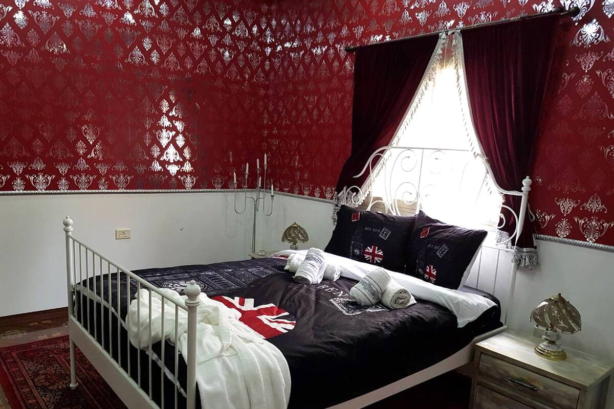 A bedroom with a bed, a nightstand, a window with curtains, and a patterned wall.