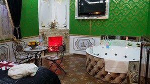 A room with a green patterned wall, a fireplace, a television mounted above it, a large bathtub, and a bed with a blanket. - Villa Jean Em (Netanya)