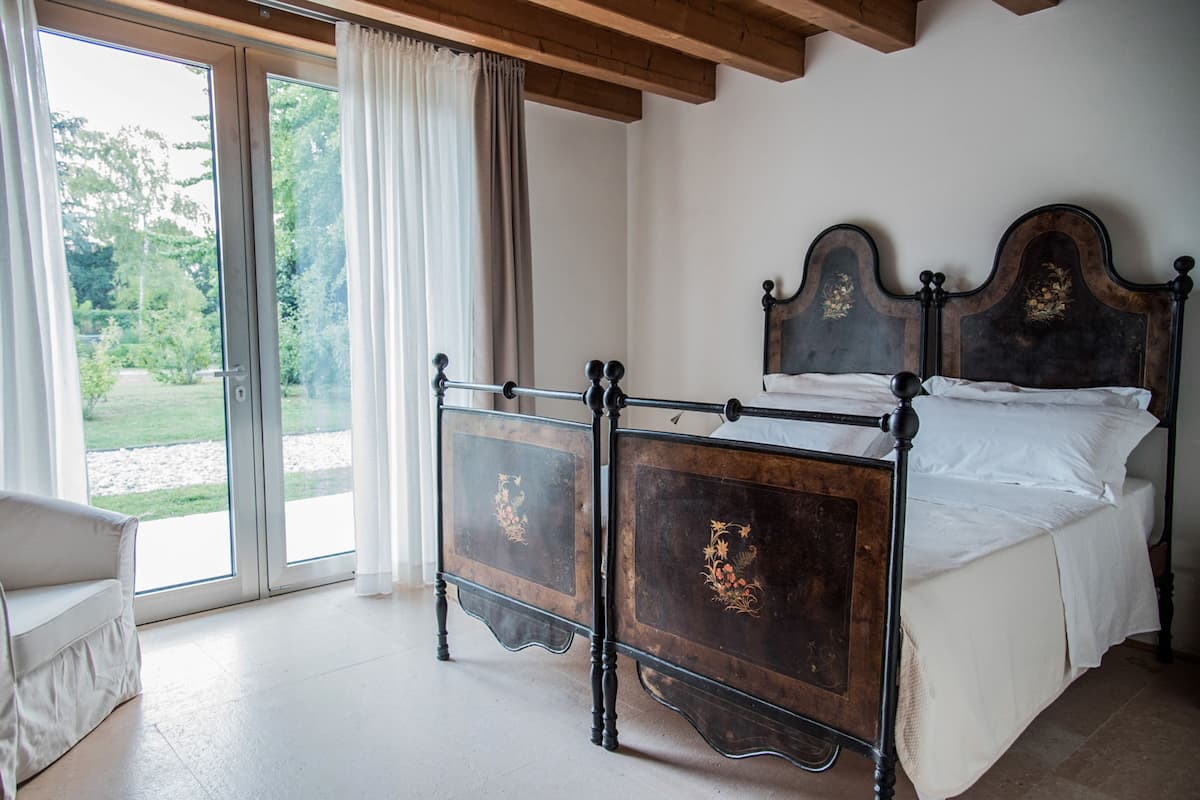 Un dormitorio con un ventanal grande, una cama con cabecera oscura y una silla blanca.