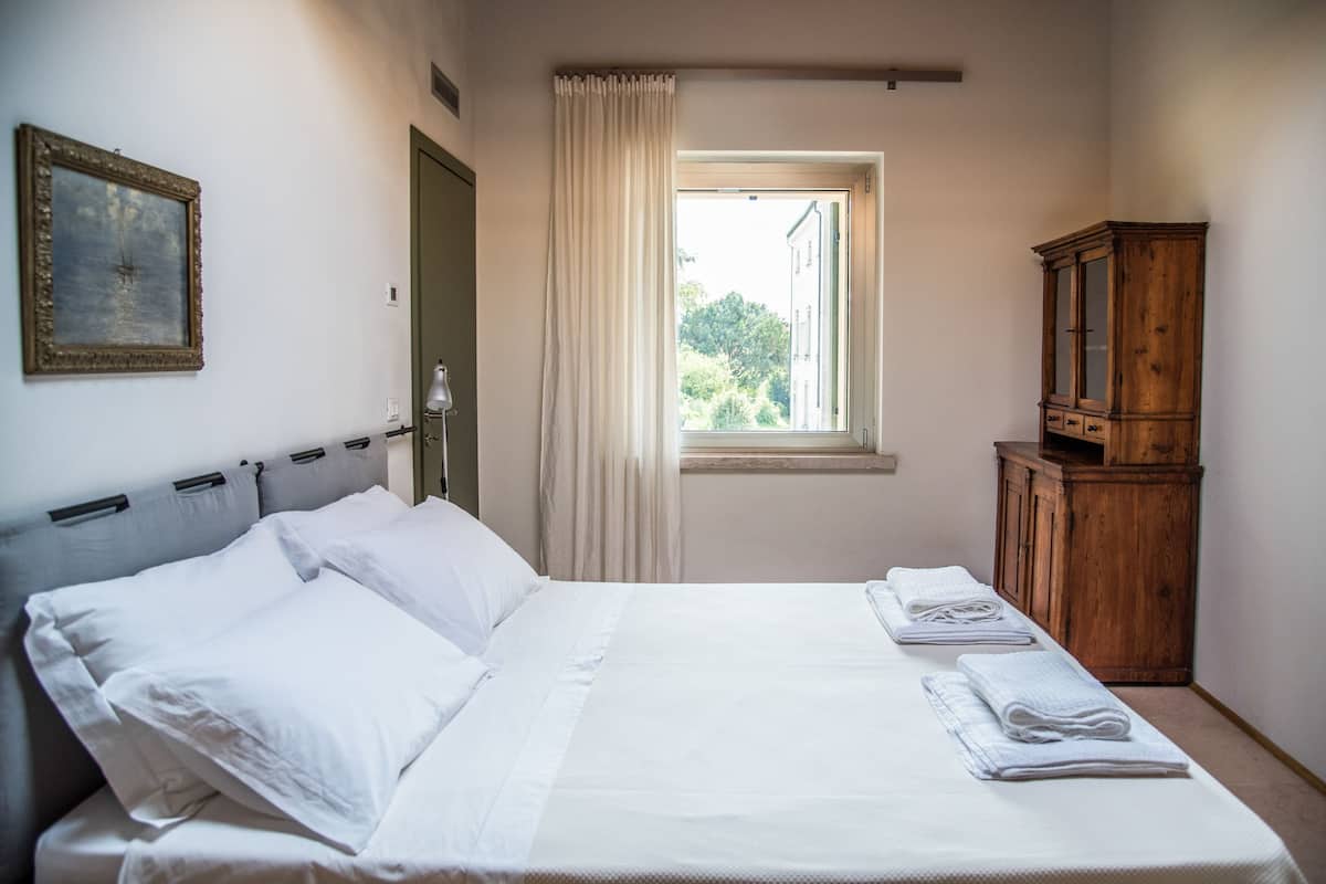 Un dormitorio con una cama, una ventana con cortinas, un armario de madera y un cuadro en la pared.