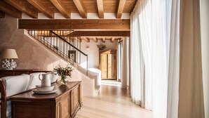 A spacious hallway with a wooden staircase, a dining area with a table and chairs, and a view of a room with a bed. - Agriturismo Corte Ruffoni (Zevio)