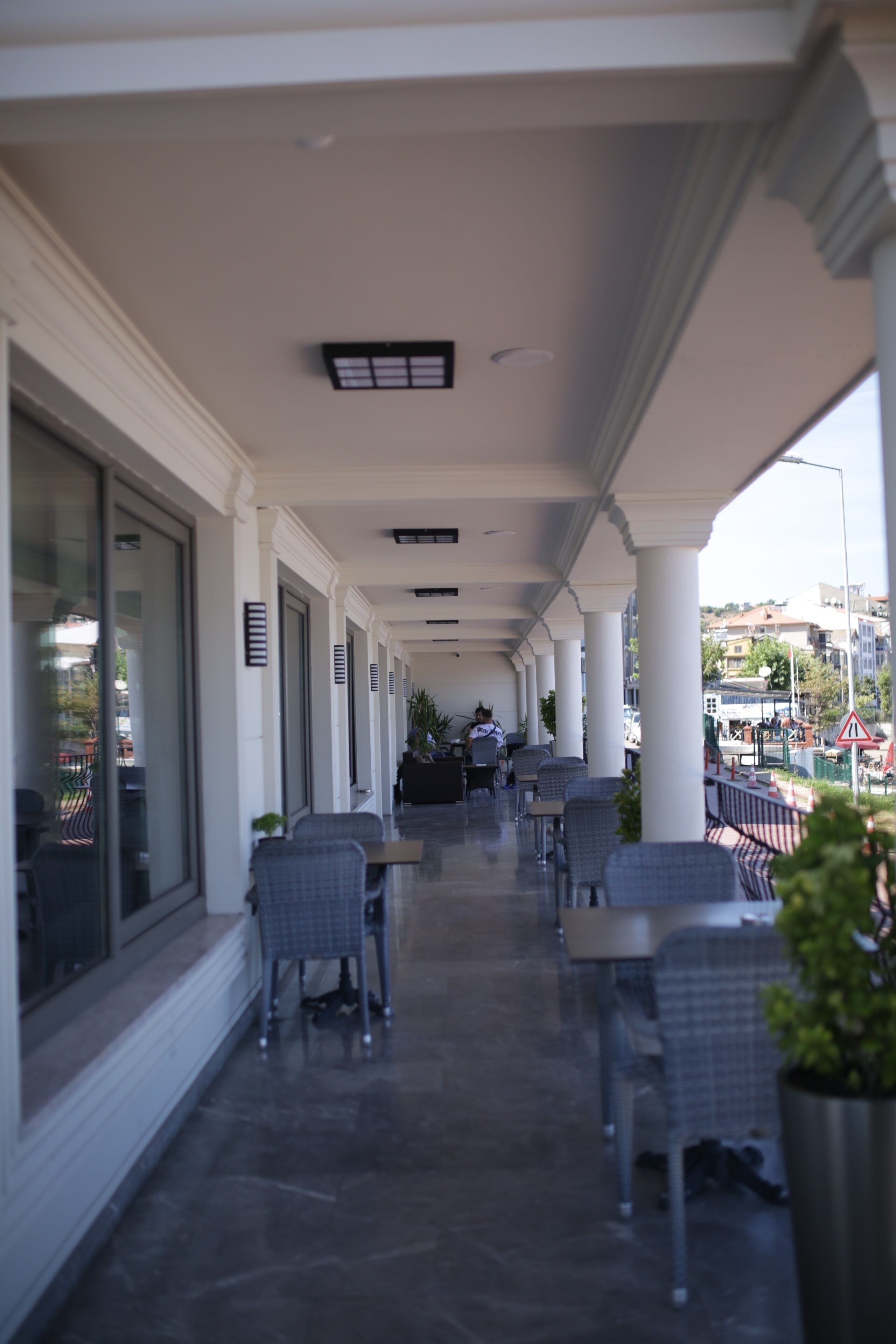 A covered outdoor seating area with tables and chairs, large windows, and a view of the street.