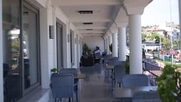 A covered outdoor seating area with tables and chairs, large windows, and a view of the street.