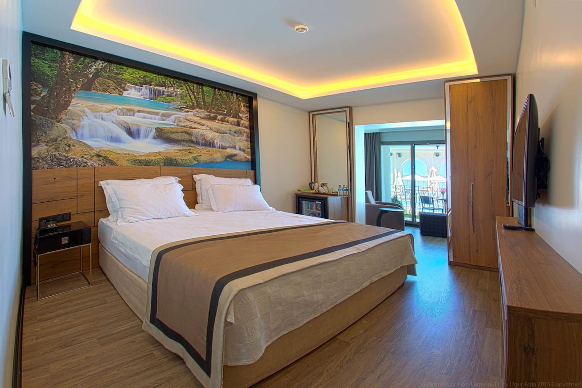 A modern hotel room with a large bed, a painting of a waterfall, a wooden desk, and a TV.