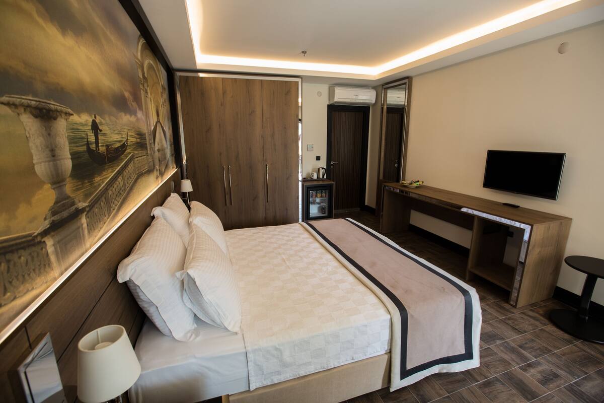 A modern hotel room with a large bed, a desk, a flat-screen TV, and a large painting on the wall.