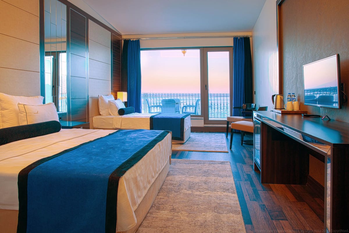 A hotel room with two beds, a desk, a chair, a TV, and a balcony with a view.