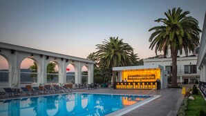 Un espace piscine avec des chaises longues, un bar et des palmiers.
