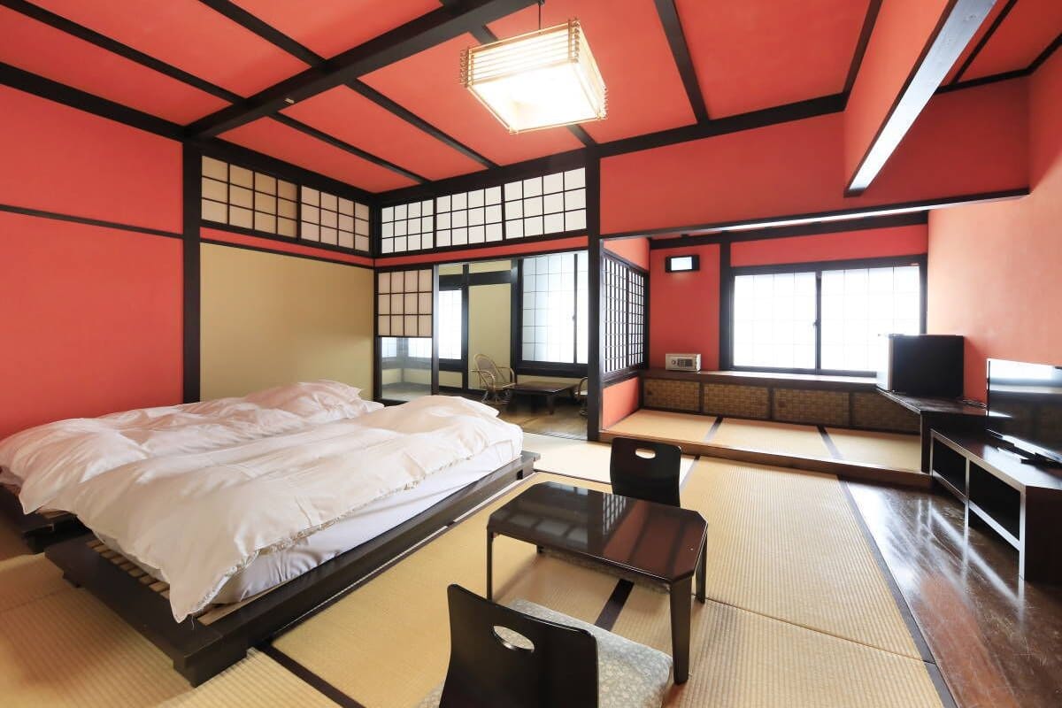 A traditional Japanese-style room with tatami flooring, a bed, a desk, and a television.