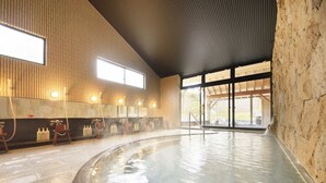 A large indoor swimming pool with a stone wall and wooden paneling on the sides. - Kaike Fuga (Yonago)