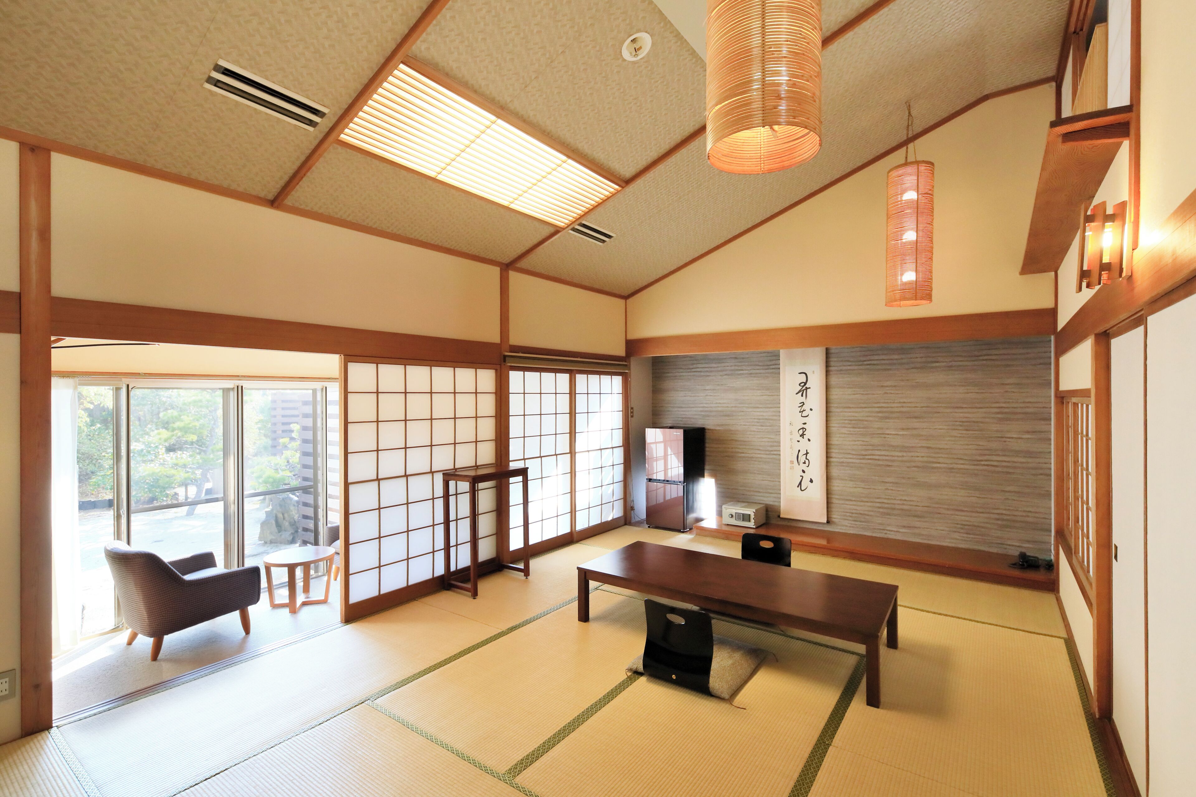 Une pièce de style japonais traditionnel, avec un sol recouvert de tatamis, une table basse, un canapé, des portes coulissantes et un téléviseur.
