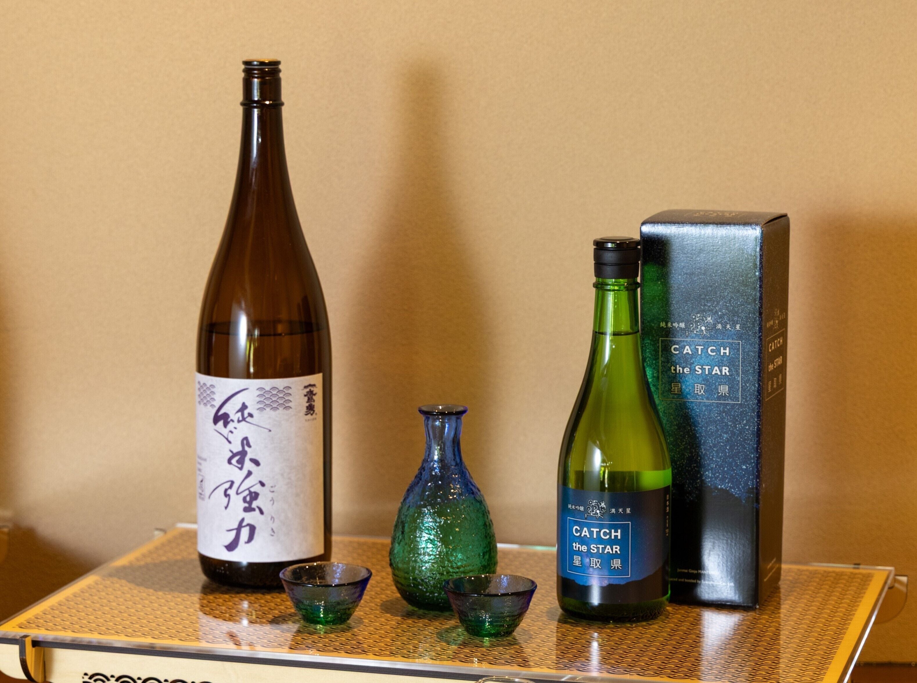 Eine Sake-Flasche, eine grüne Flasche und eine Schachtel auf einem Tisch.