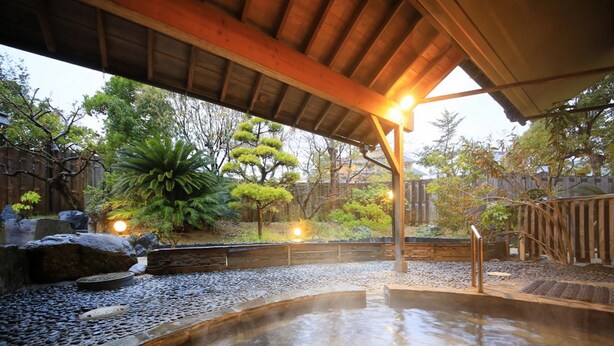 A hot spring area with a wooden deck, stone pathway, and surrounding greenery. - Kaike Fuga (Yonago)