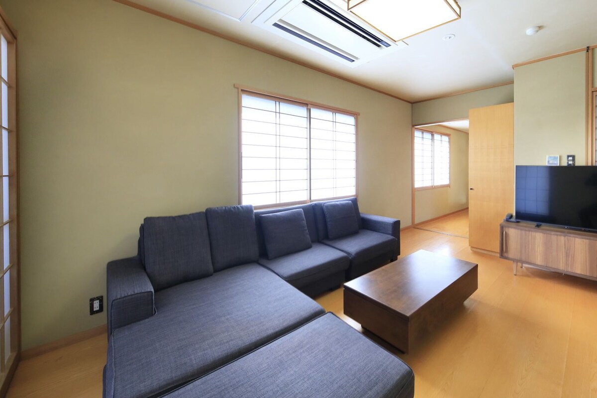 Una sala de estar con un sofá modular, una mesa de centro, un televisor sobre un mueble de madera y puertas correderas.