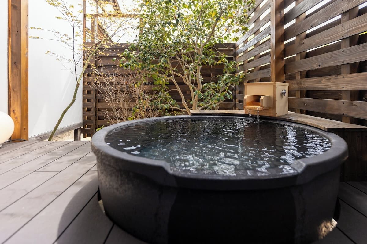 A hot tub in a wooden outdoor setting with a wooden fence and some greenery.