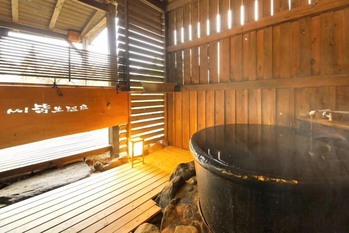 A traditional wooden bathhouse with a large black hot spring, wooden benches, and a wooden wall with a sign.