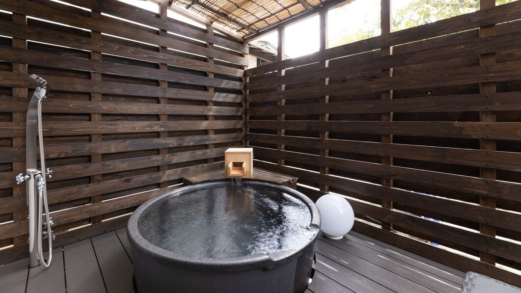 A hot tub with a wooden slatted wall enclosure, a wooden bench, and a water spout.