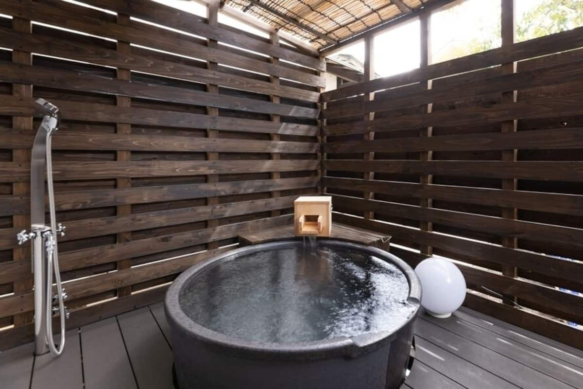 A hot tub with a wooden slatted wall enclosure, a wooden bench, and a water spout.
