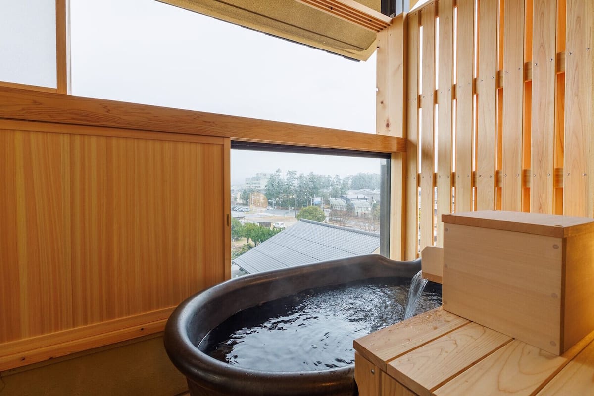 A traditional Japanese onsen with a wooden interior, a hot spring bath, and a view of the city through a window.