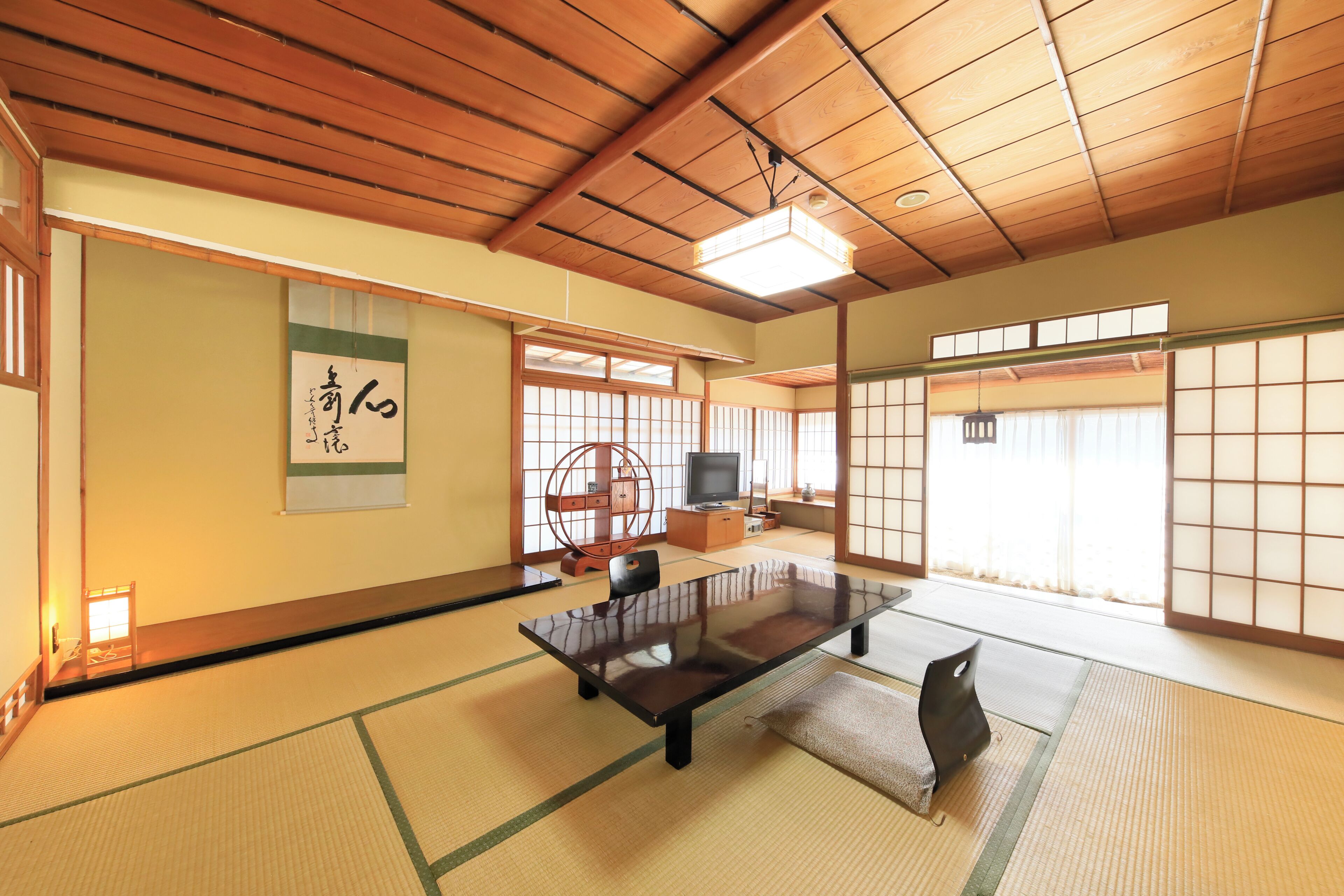 Une pièce de style japonais traditionnel, avec un sol recouvert de tatamis, une table basse, un téléviseur et des portes coulissantes.