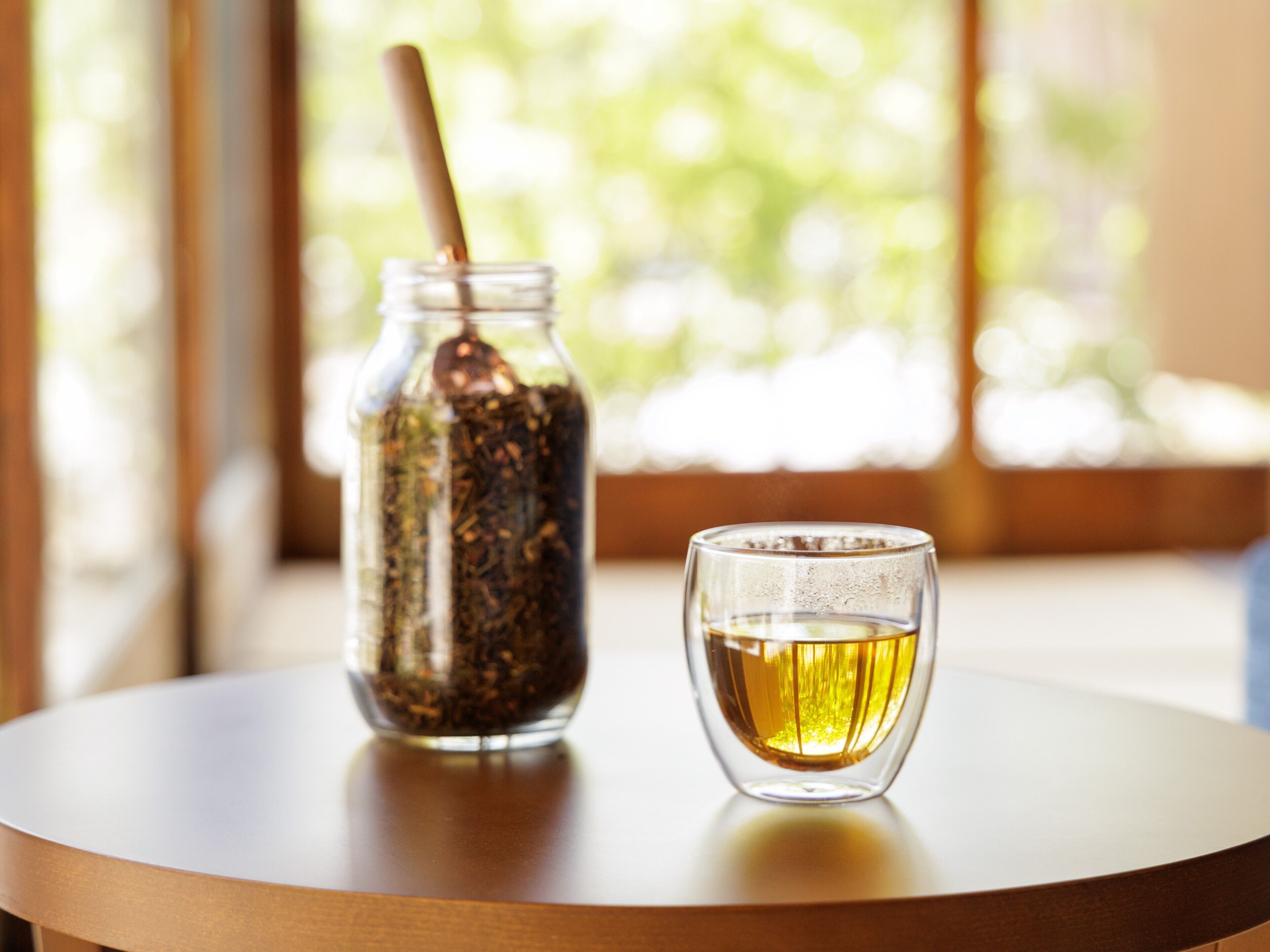 A glass jar with a spoon and a glass of tea on a round table.