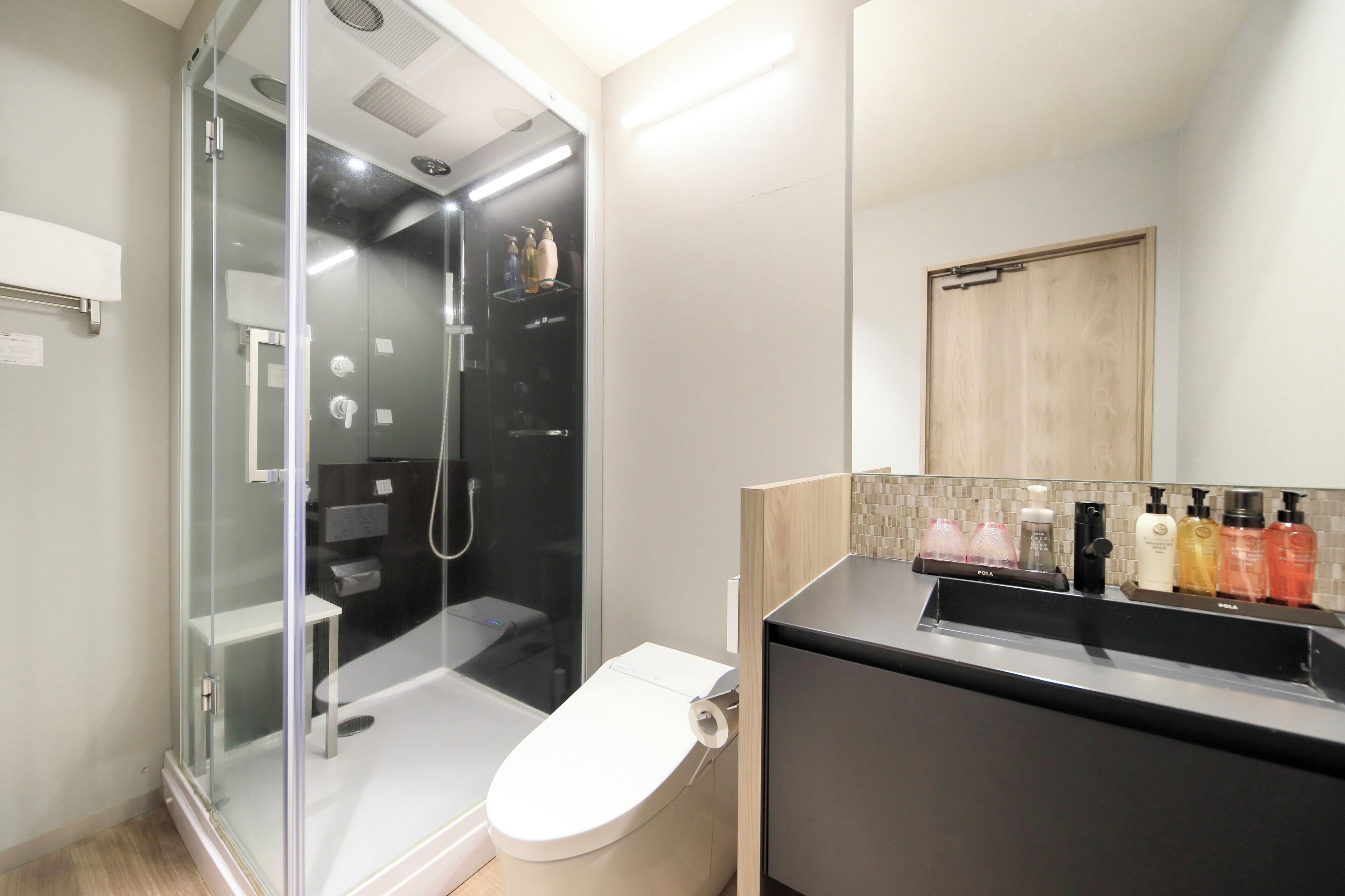 A modern bathroom with a glass-enclosed shower, a toilet, and a vanity with toiletries.