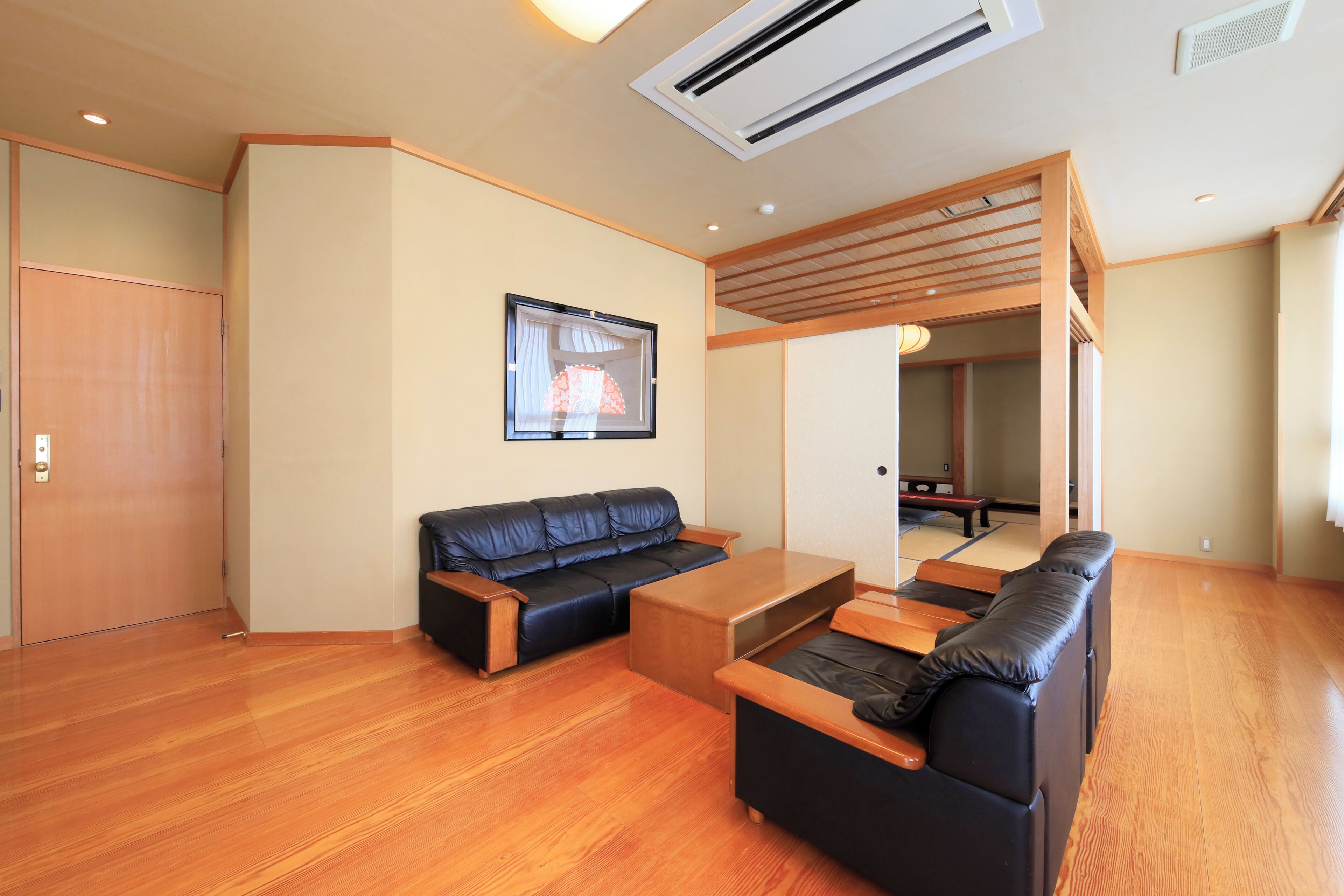 A modern living room with a black leather sofa, wooden coffee table, and a wooden bench.