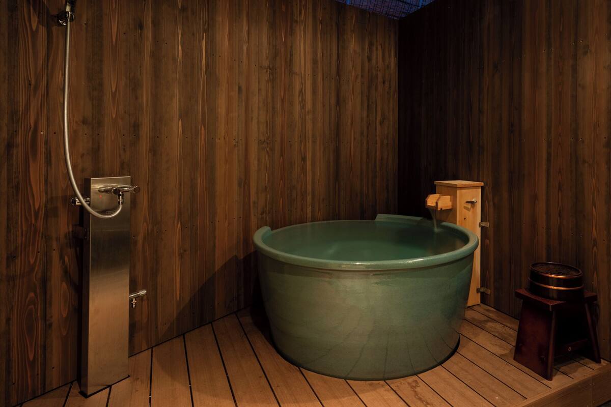 A wooden sauna room with a large green bathtub, a wooden bench, and a small heater on the floor.