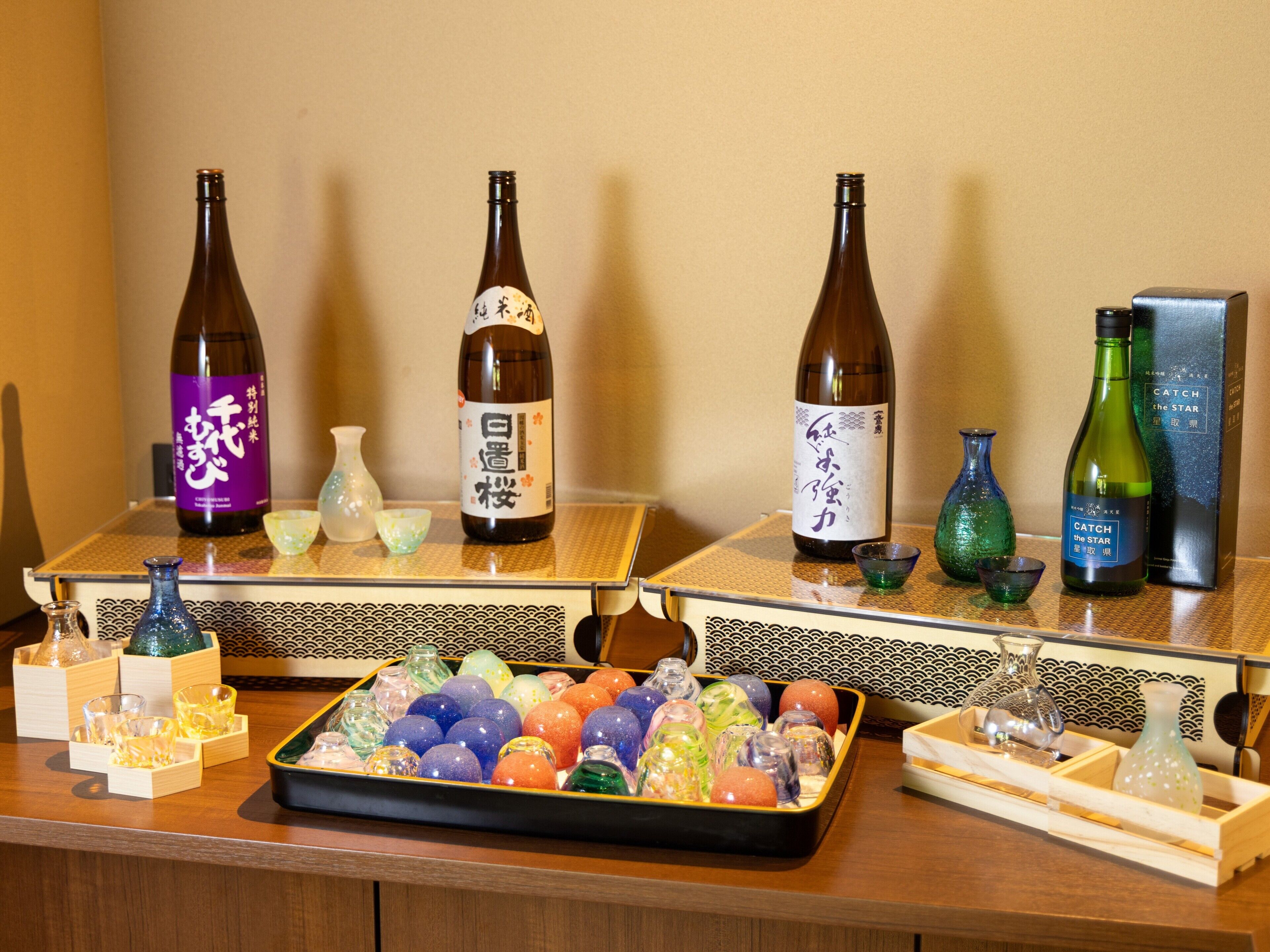 Ein Tisch mit Flaschen japanischen Sakes, einer Schale mit bunten Glasornamenten und traditionellen japanischen Vasen.