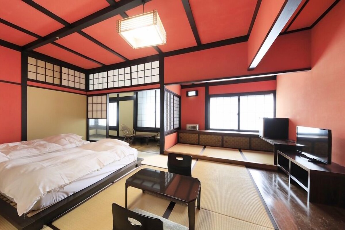 A traditional Japanese-style room with tatami flooring, a bed, a television, and a sliding door.