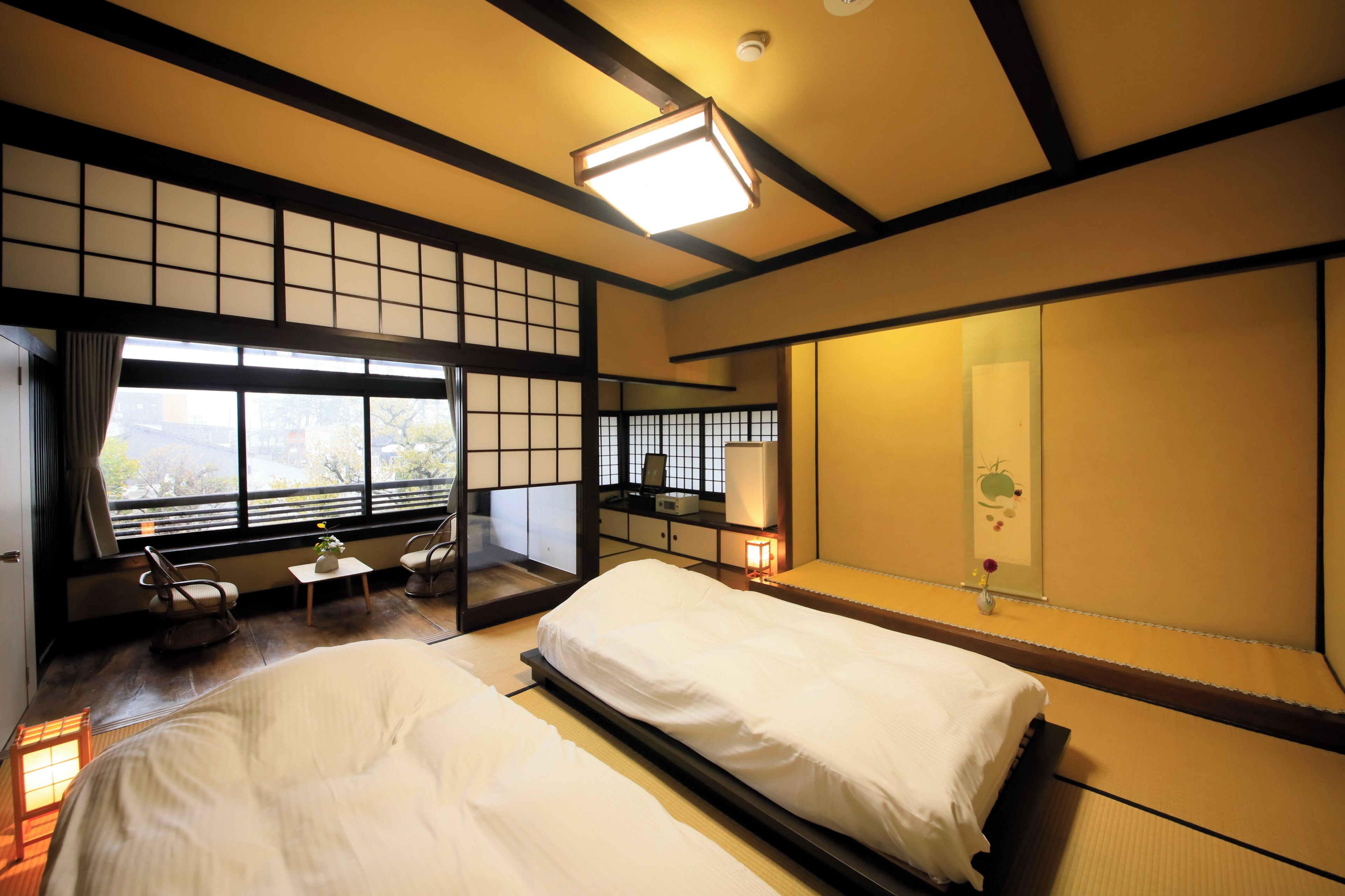 Una habitación tradicional japonesa con suelo de tatami, cama baja, escritorio con silla y un ventanal con vistas.
