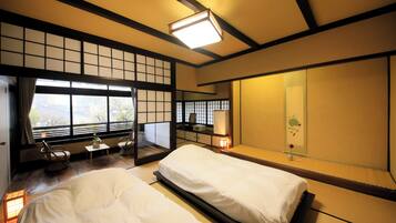 Una habitación tradicional japonesa con suelo de tatami, cama baja, escritorio con silla y un ventanal con vistas.