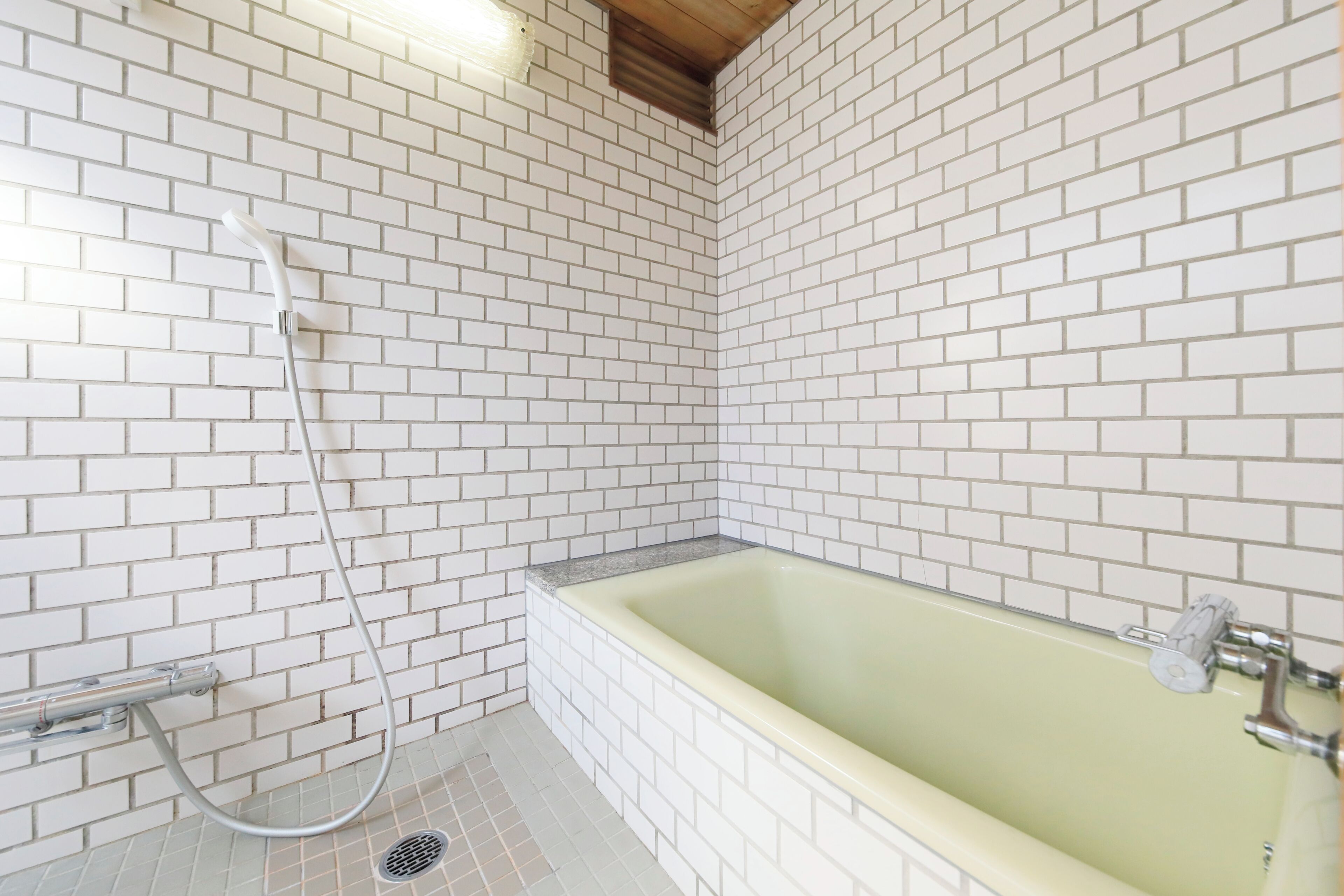 A bathroom with white tiled walls, a bathtub, and a shower.