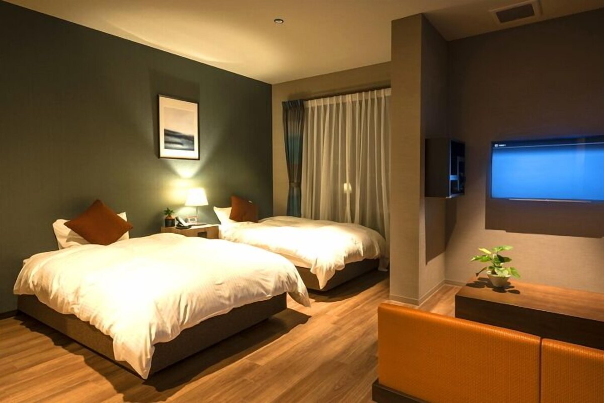 A hotel room with two beds, a desk, a TV, and a plant.