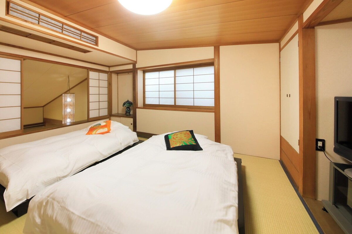 A traditional Japanese-style room with tatami flooring, two beds with white bedding, a television, and sliding doors.