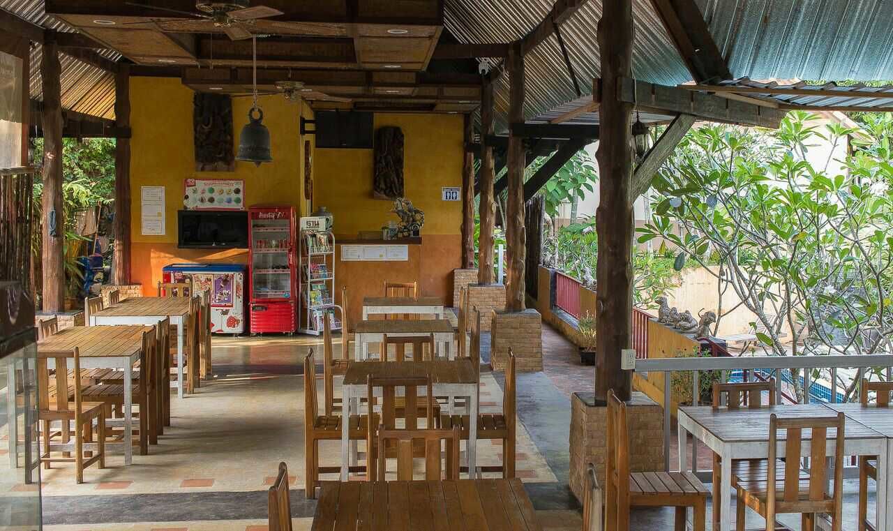 Ein Restaurant mit Holztischen und -stühlen, einer Theke mit Speisekarte und einem roten Kühlschrank.