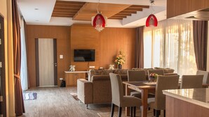 Una sala de estar moderna con sofá, mesa de comedor y sillas. Hay un televisor montado en la pared y un jarrón con flores sobre la mesa.
