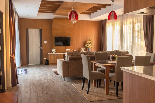 A modern living room with a sofa, dining table, and chairs. There is a TV mounted on the wall and a vase with flowers on the table.