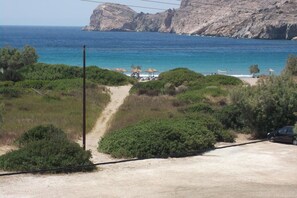 A coastal road leading to a beach with umbrellas and a few cars parked.