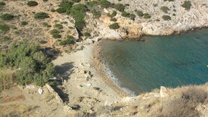 A rocky beach with sparse vegetation and a clear blue sea. - Manousos' Rooms (Syros)