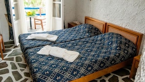 A double bed with a patterned blue and white bedspread, a wooden headboard, and a white towel folded on the bed. - Manousos' Rooms (Syros)