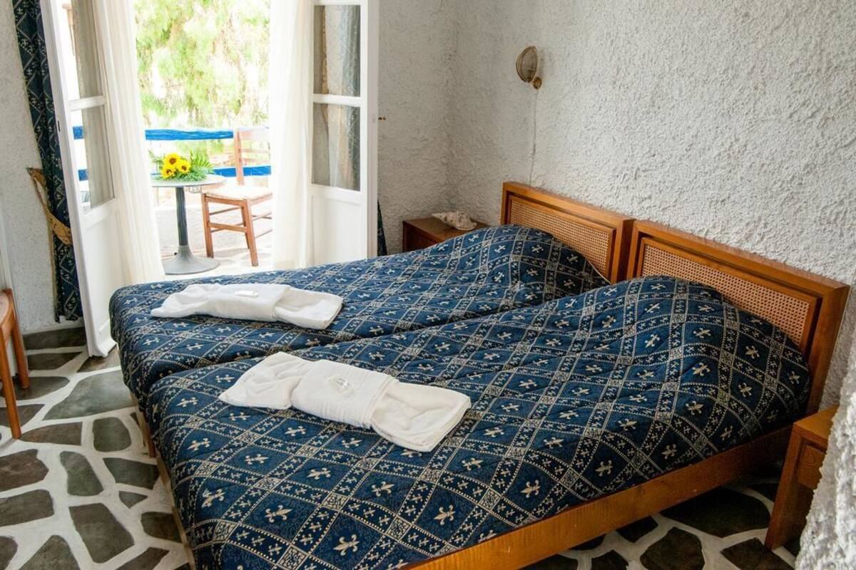 A double bed with a patterned blue and white bedspread, a wooden headboard, and a white towel folded on the bed.