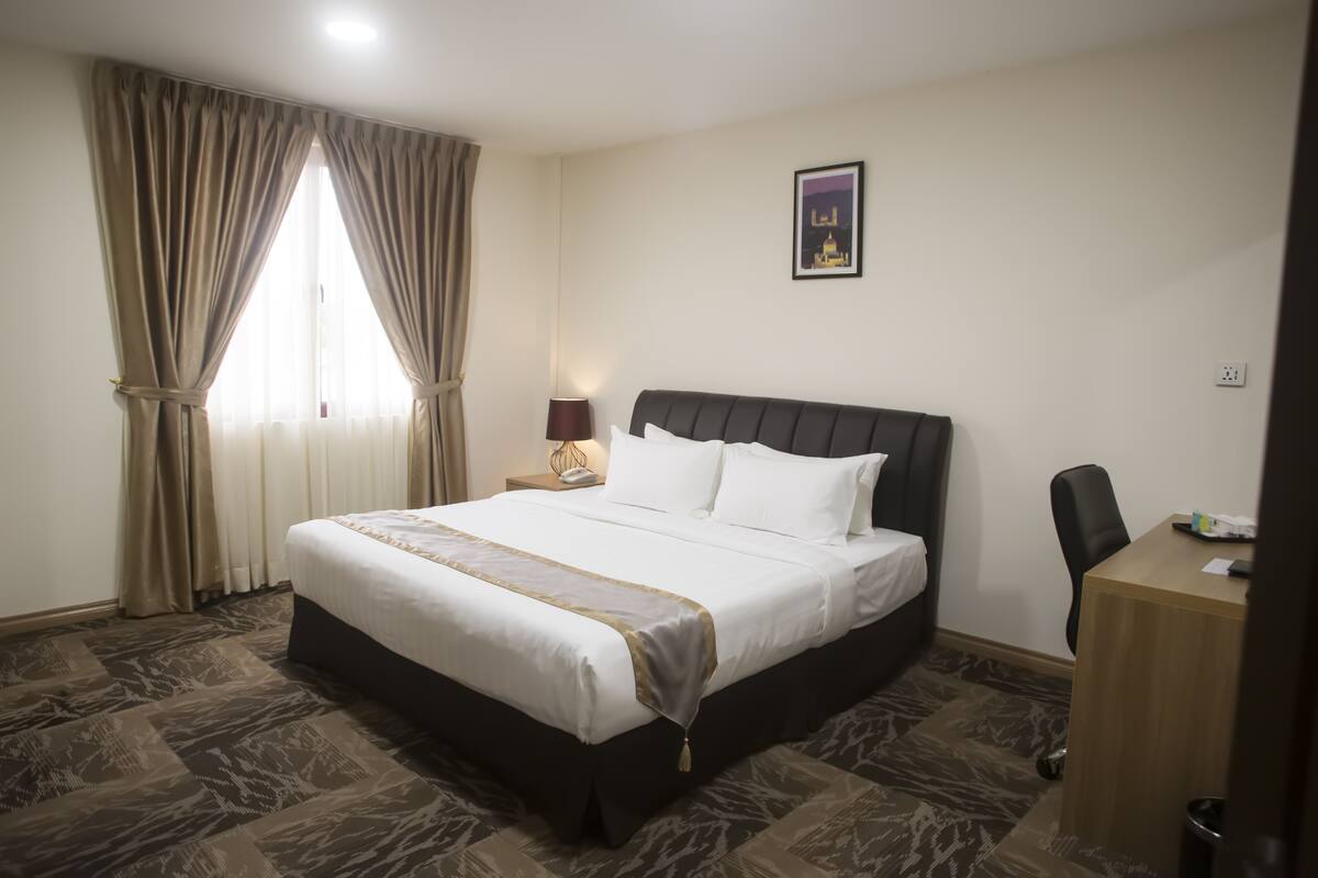 A hotel room with a large bed, a desk, and a chair.