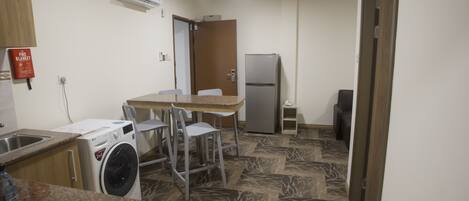 A compact kitchen with a washing machine, a refrigerator, and a dining area with chairs.