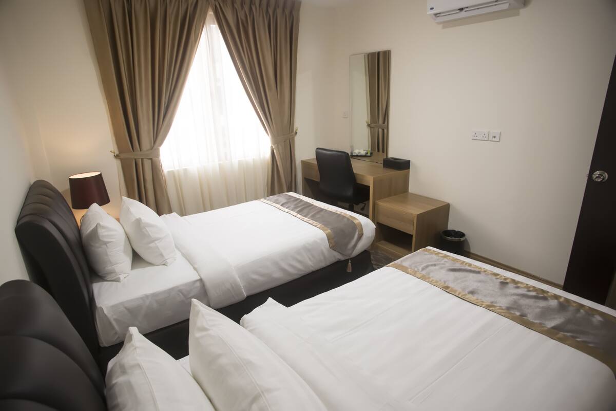 A hotel room with two beds, a desk, a chair, a lamp, and a window with curtains.