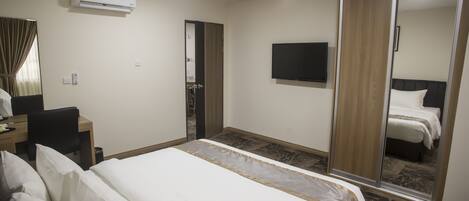 Habitación de hotel con cama, escritorio, silla, televisor y armario.